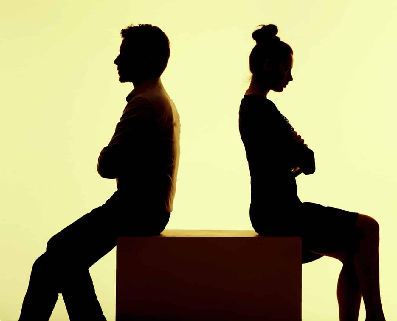 silhouette man and woman sitting back to back on a box with arms folded