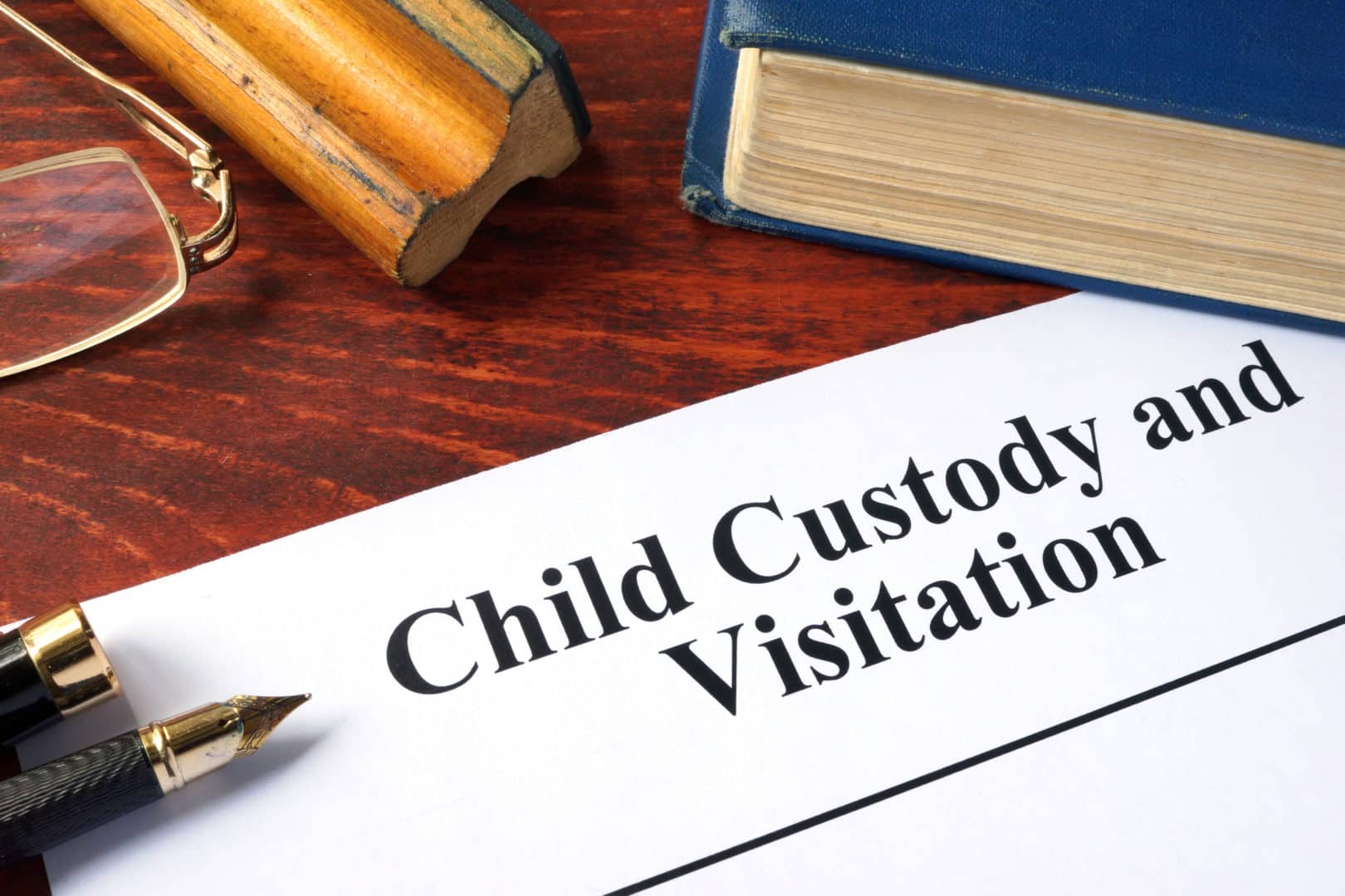 paper with child custody and visitation with a book, pen, and glasses on a wooden table