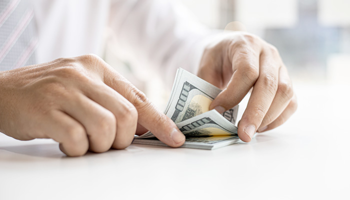 A businessman counting his dollar bills on a white table counting the money to invest in the funds and stocks