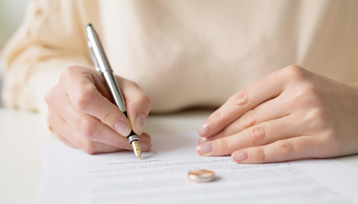 woman signing document with wedding ring on the table